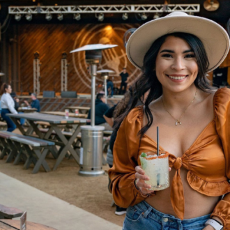 2022AugustEvents, Women in cowboy hat, orange silk top, and blue jeans holding a margarita at the Rustic in San Antonio