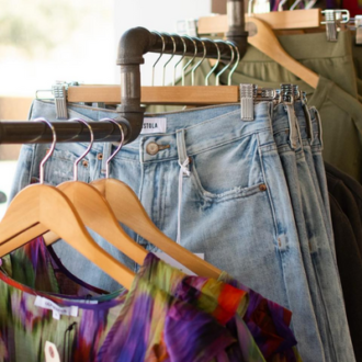 A rack of clothes with three levels, first with a multicolored sheer top, then with blue jeans, then with a green two-piece set