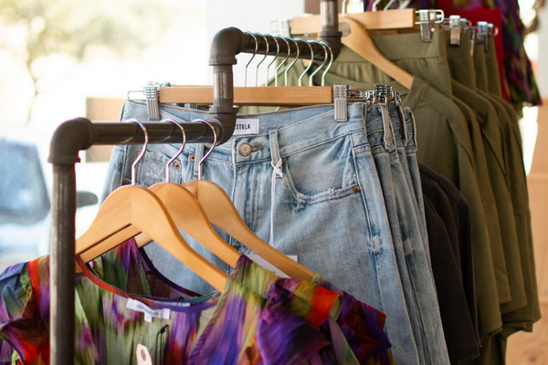 A rack of clothes with three levels, first with a multicolored sheer top, then with blue jeans, then with a green two-piece set